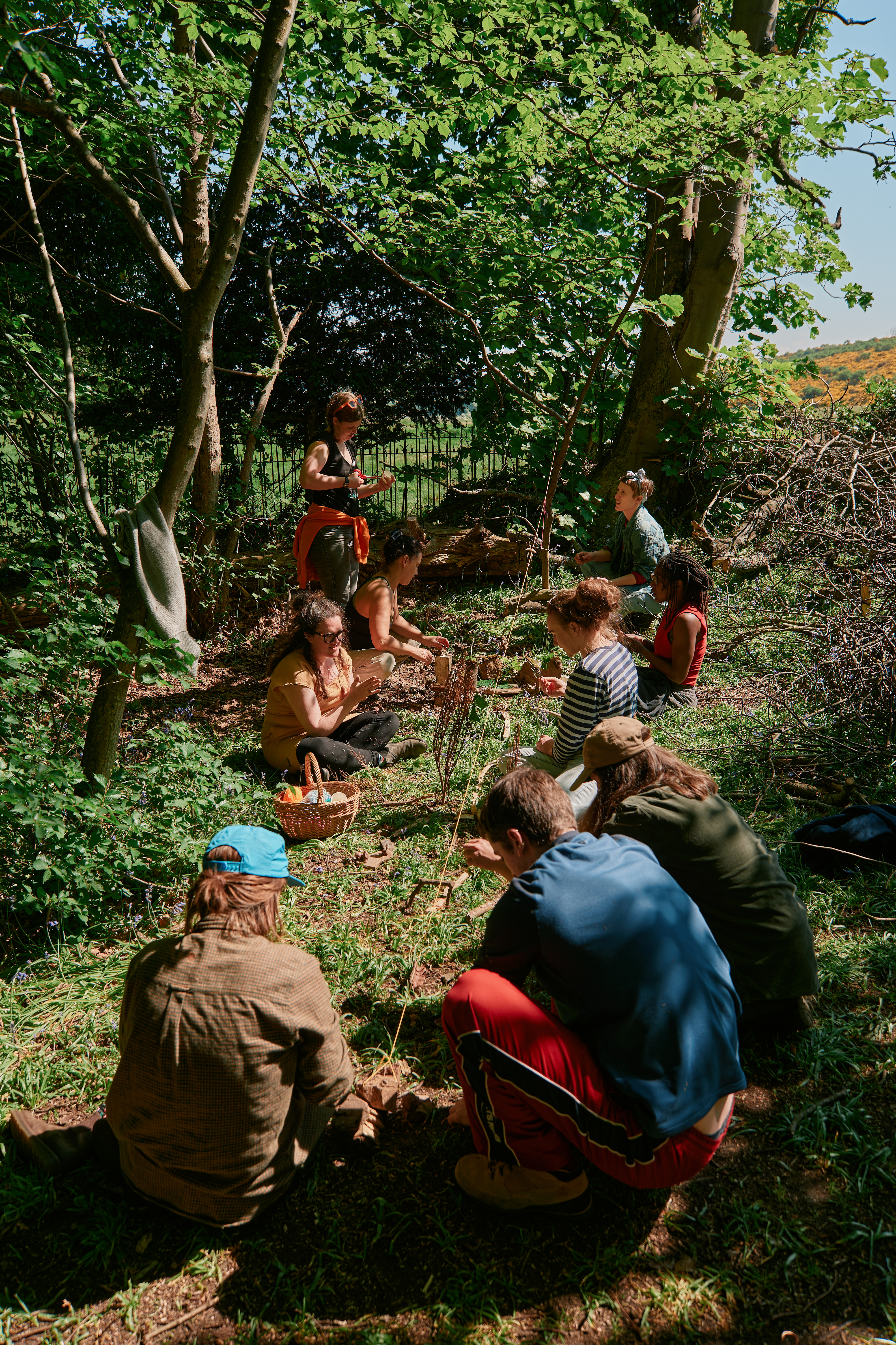 Nine people sitting on some grass in the woods doing an activity together