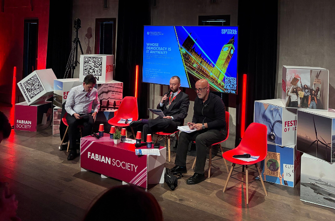 Panel discussion on a stage with four seated speakers around a table with red lighting.